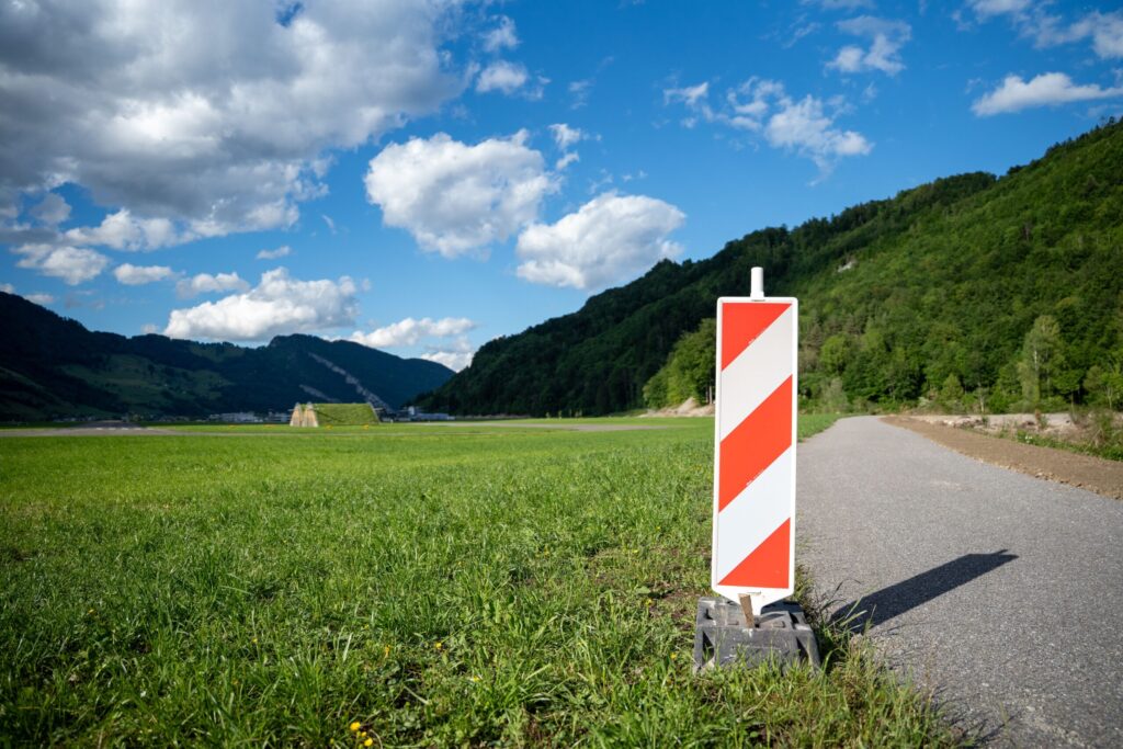 Road barrier against lush green landscape in Alpnach, Switzerland under a bright blue sky.